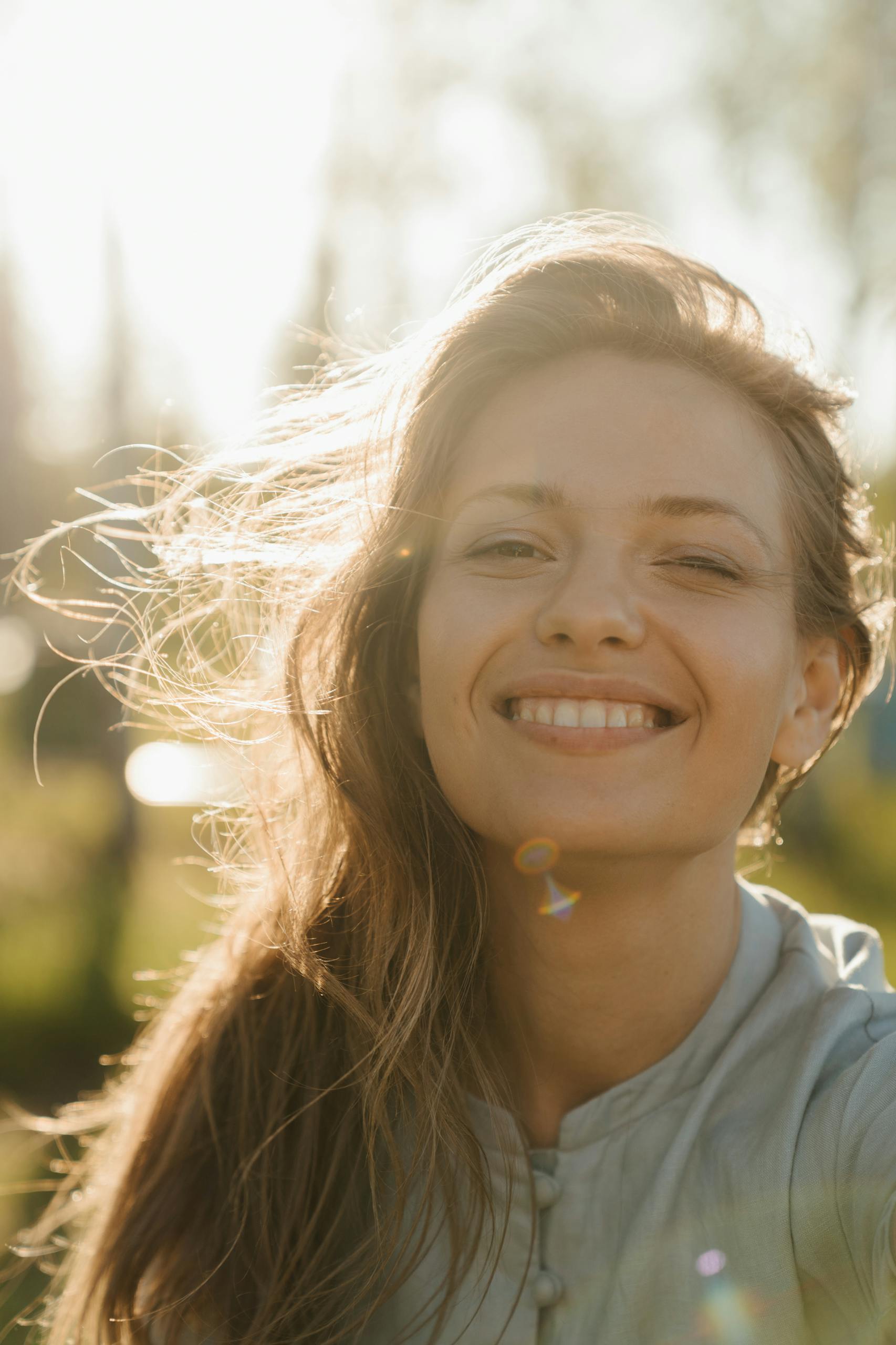 A radiant woman smiling in the sunlight with hair gently blowing outdoors.
