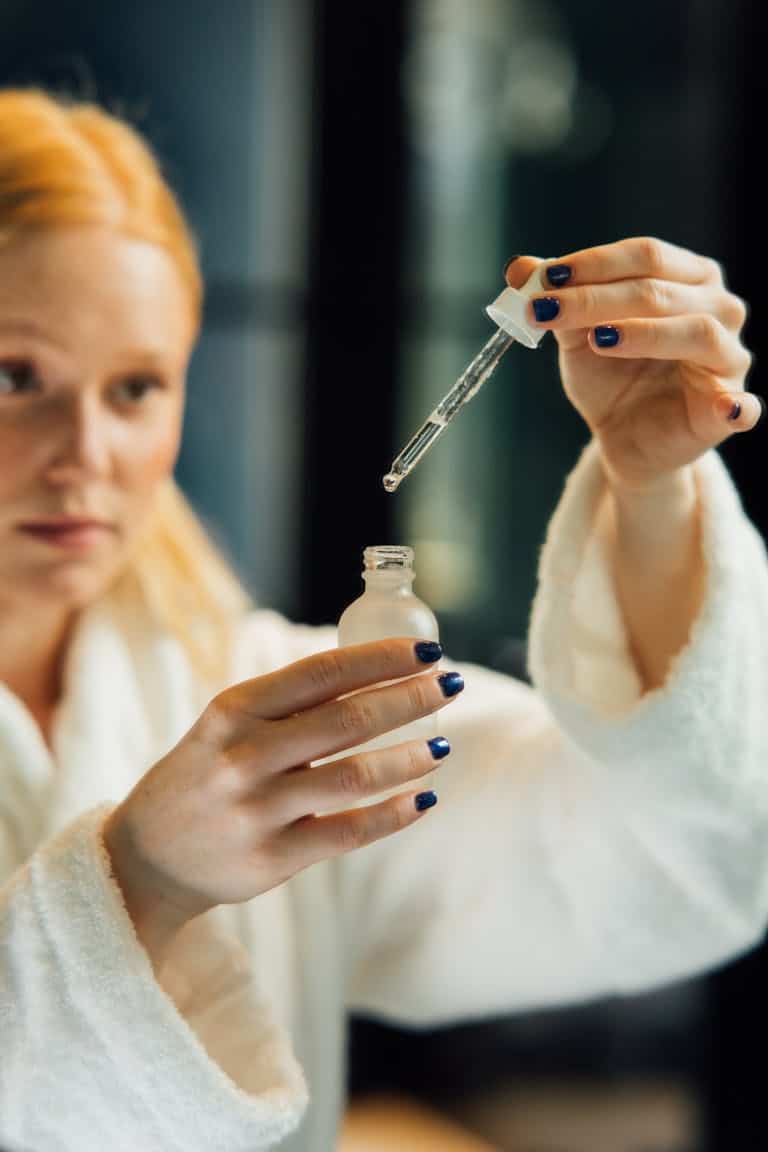 perimenopause skin redness Blonde woman in a bathrobe applying serum with a dropper for skincare routine.