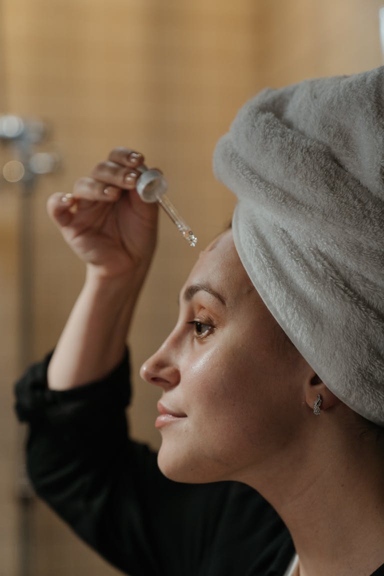 perimenopause skin care routine Close-up side view of a woman applying skincare serum with a dropper, promoting beauty routine.