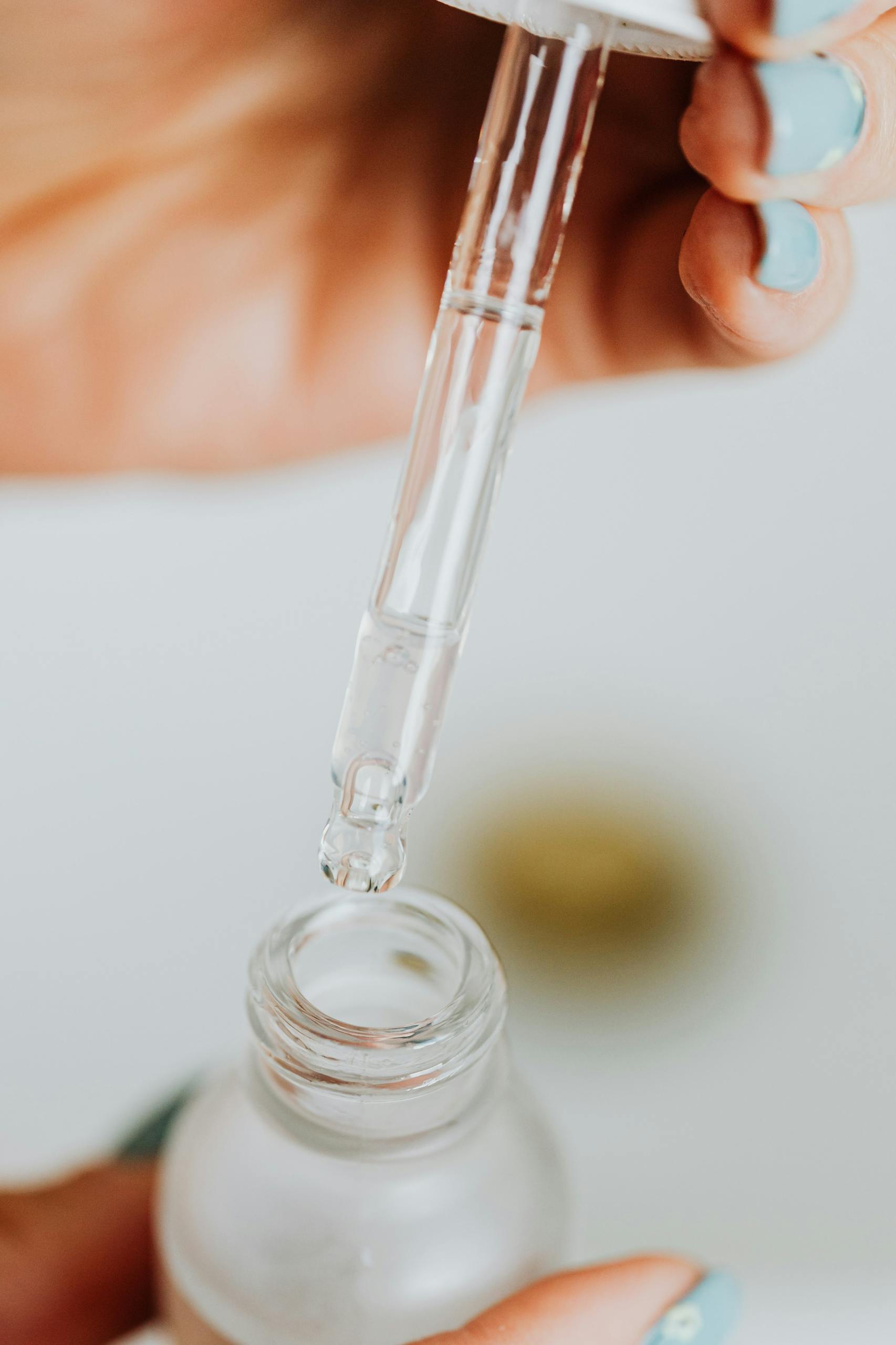 Detailed close-up of a dropper dispensing liquid into a glass serum bottle for skincare routine.
