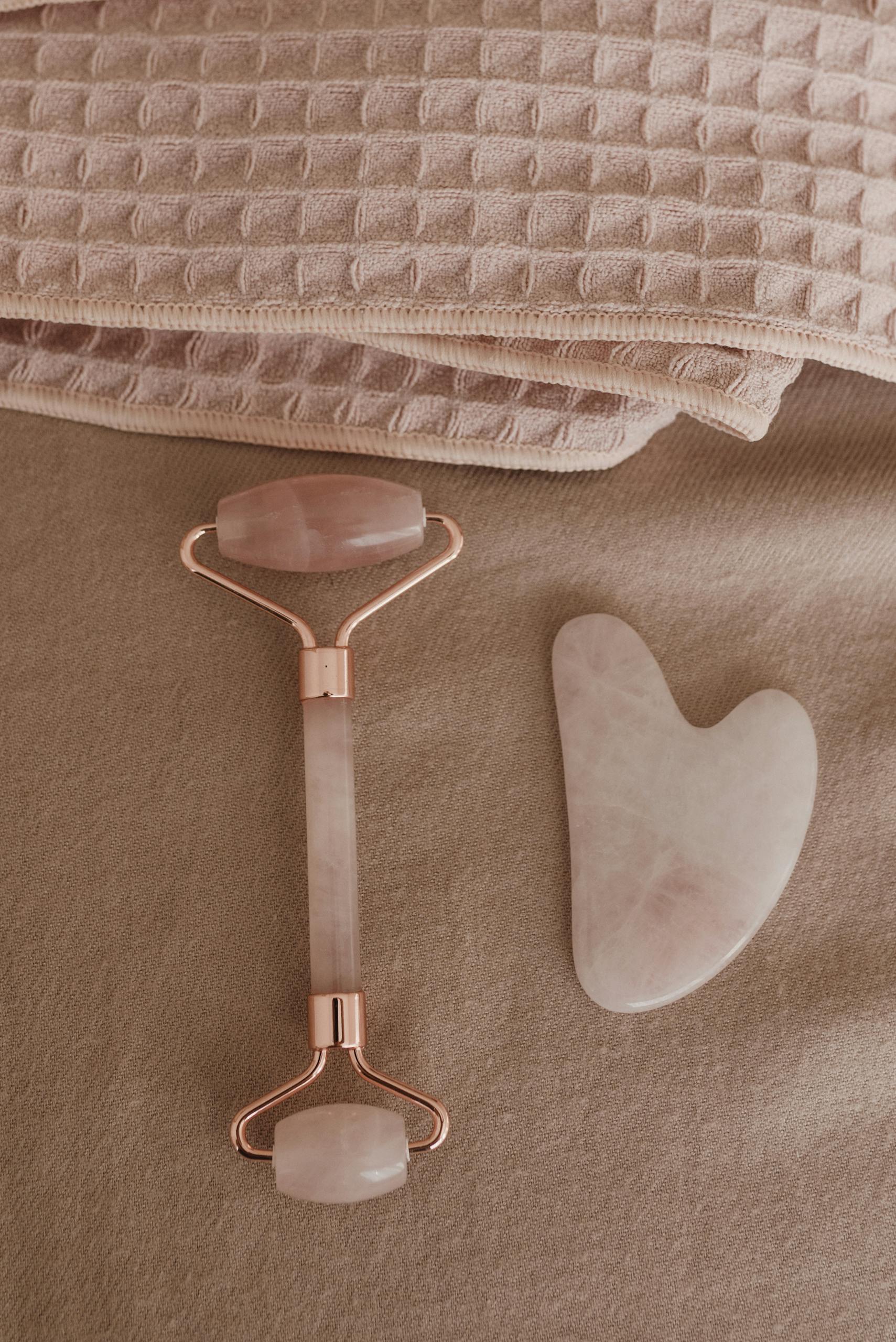 Flat lay of a rose quartz skincare tool set and towels for a wellness routine.