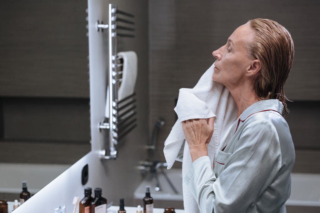 Cleanser for perimenopausal skin, woman in a bathroom, drying her face with a towel during her morning skincare routine.