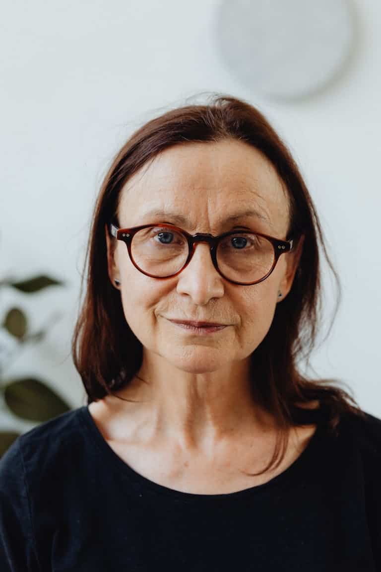 Portrait of an elderly woman wearing glasses and a black shirt, looking directly at the camera.