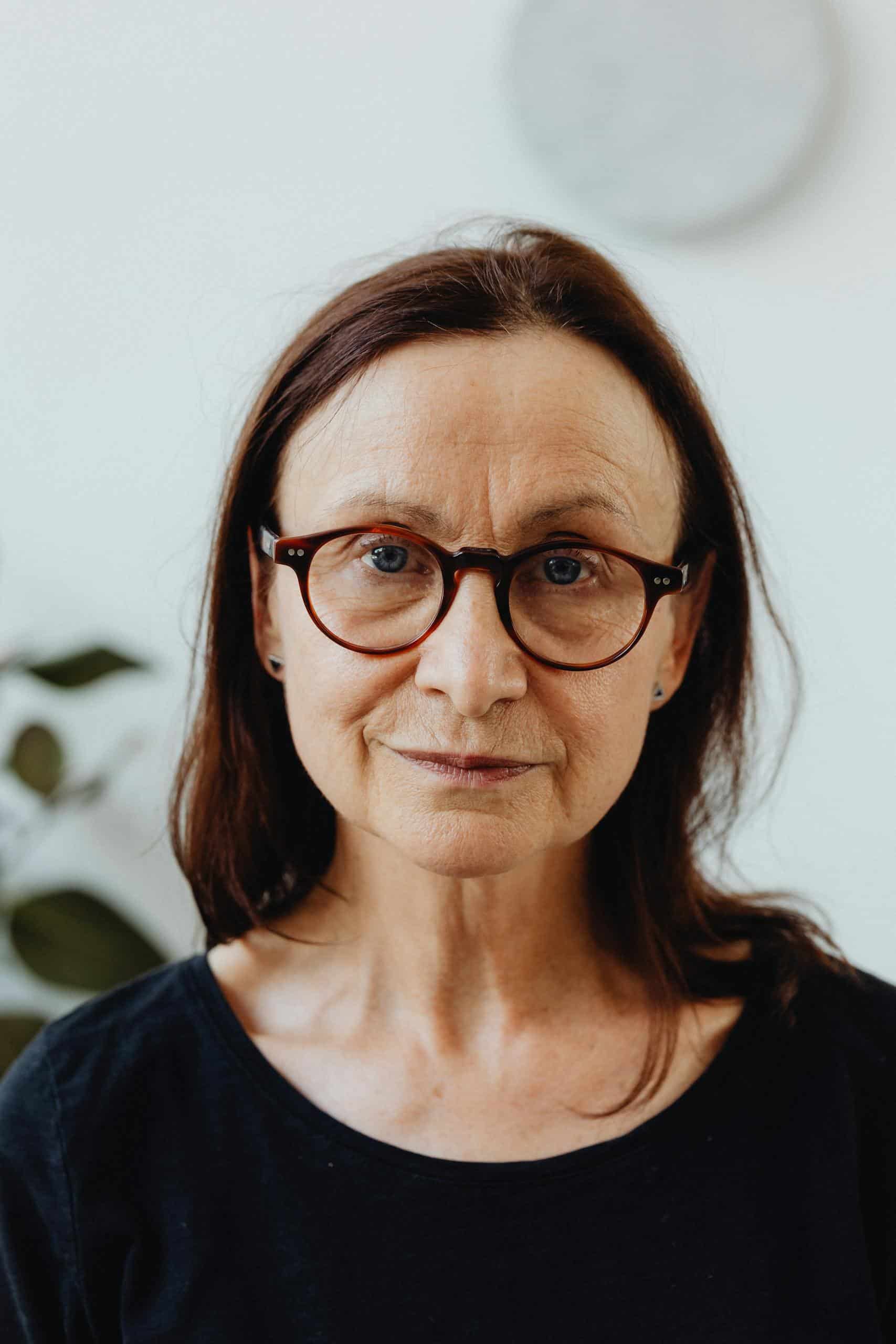 Portrait of an elderly woman wearing glasses and a black shirt, looking directly at the camera. Treating 11 lines without botox