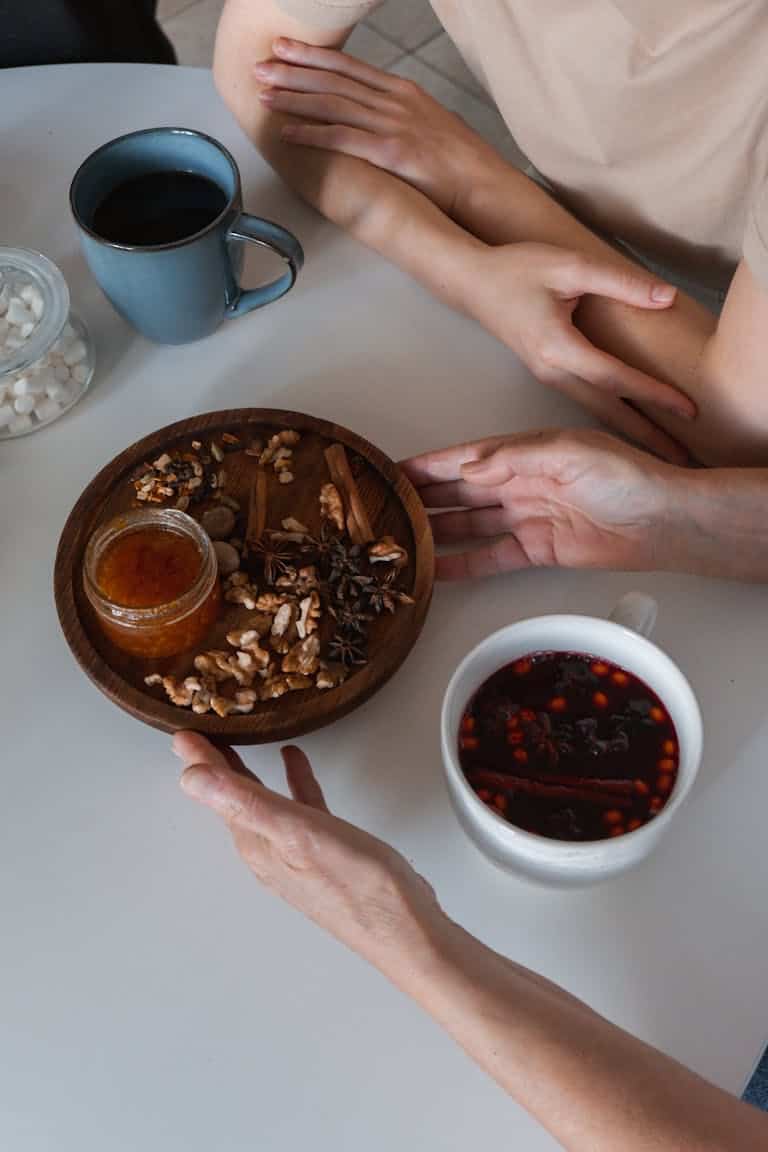 High angle shot of nuts, coffee, and spices on a white table with hands present.