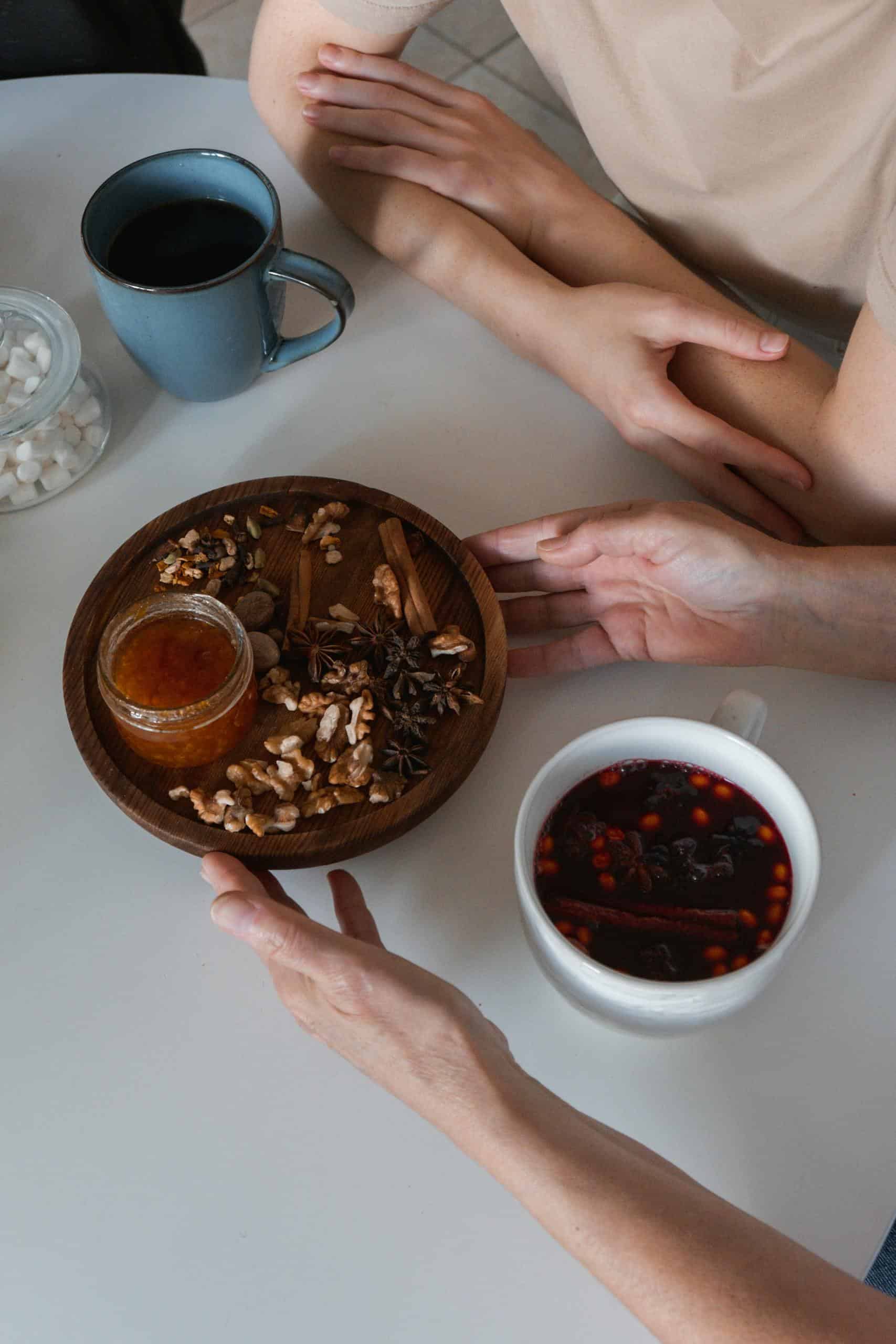 High angle shot of nuts, coffee, and spices on a white table with hands present.